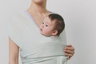Baby looking to the side from an Apple Mint Konny Baby Carrier FLEX AirMesh™ on a parent's chest, plain light grey wall