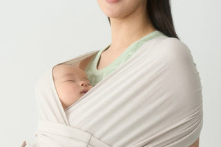 Sleeping newborn wrapped in a cream Konny Baby Carrier FLEX SoftBreeze™ on a parent's chest, light wall