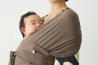 Baby resting on a parent's chest in a brown Konny Baby Carrier FLEX SoftBreeze™, plain light background