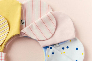 Konny cloth baby bibs in stripe, solid and dot prints laid in a circle on a pink background
