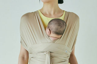 Baby on a woman's chest in a Honey Beige Konny Baby Carrier FLEX AirMesh™ tied at the waist, over a yellow top