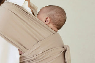 Baby asleep on a parent's chest in a beige Konny Baby Carrier FLEX SoftBreeze™, plain studio wall
