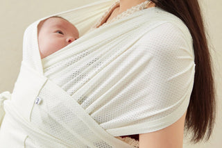 Wide-eyed newborn snug on a woman's chest in a Cream Konny Baby Carrier FLEX AirMesh™, beige wall