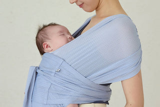 Sleeping newborn held in a light blue Konny Baby Carrier FLEX AirMesh™ against a plain grey wall