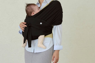 Baby snug on a woman's chest in a Black Konny Baby Carrier FLEX SoftBreeze™, over a light blue shirt, plain light wall